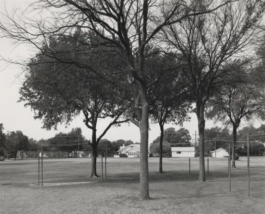 Black and white photograph of a school yard with a  small field and bare trees. 
