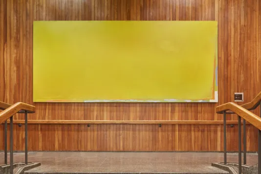 Large yellow painting on a wood paneled wall with staircases on the left and right. 