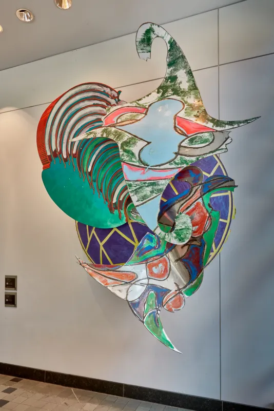 Colorful sculpture made of acrylic and enamel on aluminum hung on a white wall. 