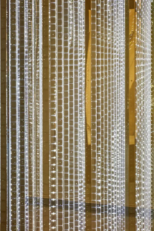 Detailed view of a sculptural work made of stainless steel rods that hang vertically with LED lights on the surface. 