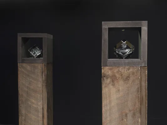 Small laser-cut glass cube sculptures nested inside the top section of brown pedestals.