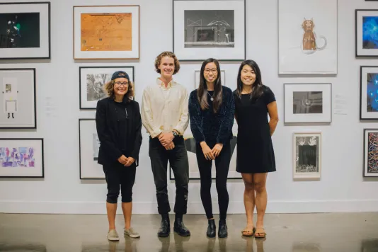 Four student guides stand in the gallery with a salon style hang on the wall behind them.