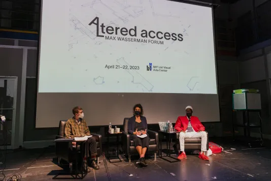 Three Altered Access participants sit on a stage in a panel discussion. Behind them is a bright projector screen that reads "Altered Access, 2023 Max Wasserman Forum" with the forum dates below and the MIT List Visual Arts Center logo. 