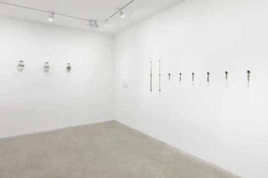 The corner of a white walled room with a row of three glass jars hung on the back left side wall and a row of eight test tubes that are hung on the right side wall.