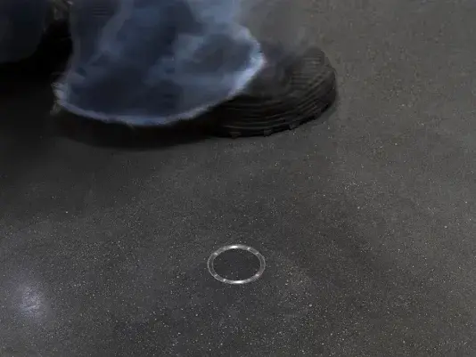 A small metal ring is cemented into the floor. Someone wearing a black sneaker and blue jeans is walking behind the metal ring.