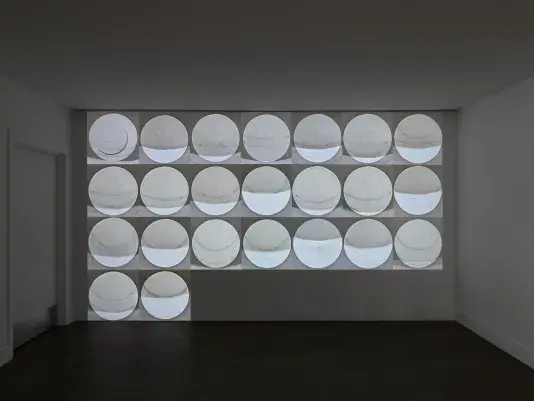 Black and white video of a series of images of the sun in a grid is projected onto a white wall. 