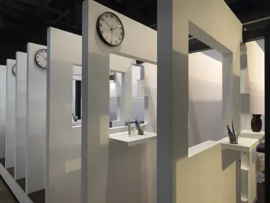 A series of white walls with a window cutout has a view of the next white wall with a window cutout. There is an analog clock hanging at the top left corner on every wall.