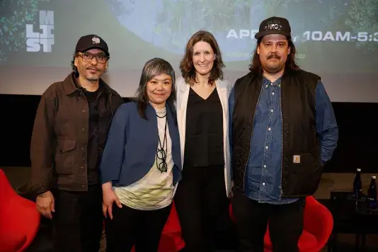 A group of four people standing in a row on stage in front of a projector screen.