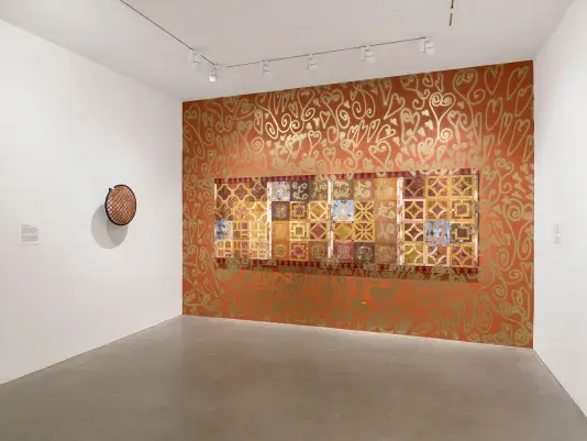 A tile-like painting hangs on an orange wall decorated with gold spray-painted motifs. To its left, a painted security mirror is mounted on a white wall.