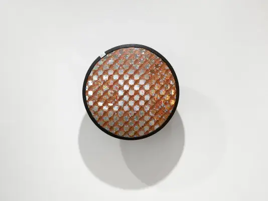 A round convex security mirror is covered by an interlocking brown star pattern created by intersecting notched lines. The pattern is adorned with delicately painted flowers.