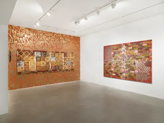 A tile-like painting hangs on an orange wall decorated with gold spray-painted motifs. To its left, a painted security mirror is mounted on a white wall. To its right another tile-like red painting hangs on the wall.