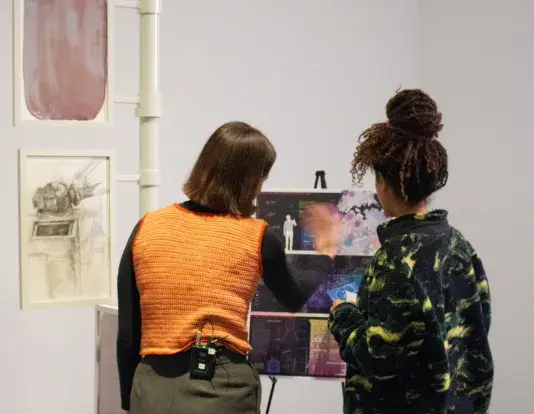 Two young women looking at a poster board depicting research for pigeon politics in a gallery space at the MIT List Visual Arts Center.