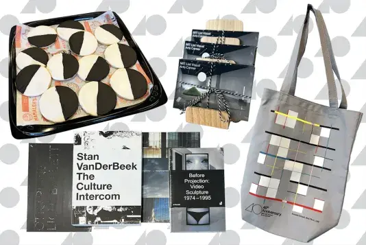 Four exhibition publications are in the bottom of the frame. A tray of black and white cookies is to the left, a rack of postcard sets is in the upper middle and a gray tote bag is to the right, all in front of a white background with gray triangle and circles repeated design.
