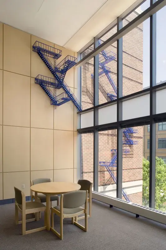 Blue sculpture created out of multiple ladder forms. The ladder begins inside and continues outside the building window.
