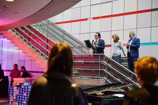 List Center Director Paul Ha gives remarks from a set of stairs to a crowd. Next to Paul are two people toasting the occassion.