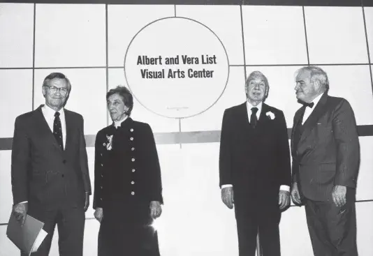 Black and white photograph of four people standing in front of a wall. There is a circle sign with text in the middle that reads "Albert and Vera List Visual Arts Center"