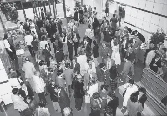 Black and white photograph of an aerial view of a large crowd of people gathering in the atrium lobby of a building.