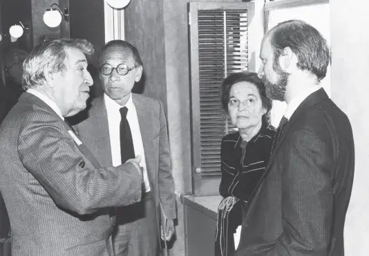 Black and white photograph of four people in conversation standing in a circle.