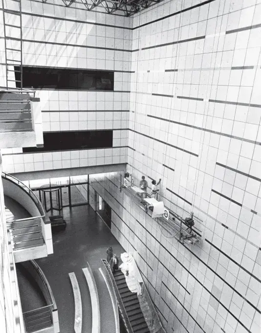 Black and white photograph of an open atrium from the third floor window with geometric patterned walls and a stairwell in the center of the first floor.