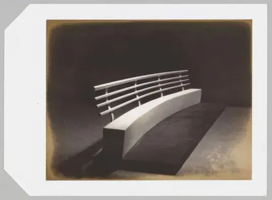 Black and white image of a curved bench with a dark surrounding.