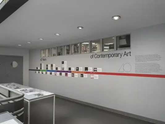 A large vitrine encasing black and white photos in the middle of an open atrium. A colorful timeline with images is adhered on the wall behind.