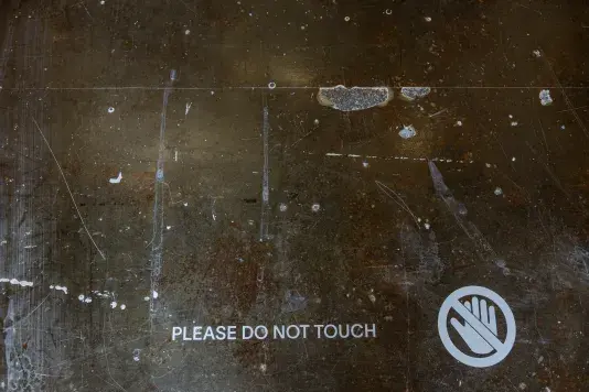 A dark floor, marked with scratches and drips of white paint, displays the white text 'PLEASE DO NOT TOUCH' next to a white circular symbol of a hand with a diagonal line through it.