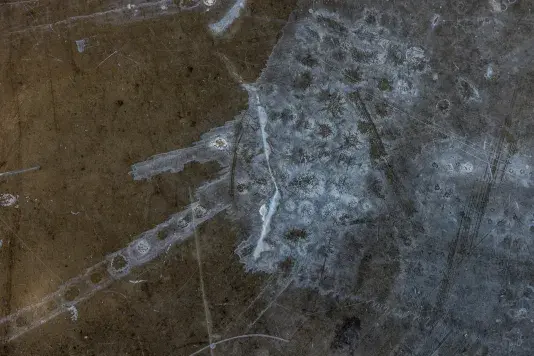 A dark, textured floor with white and gray residue, streaks, and numerous fine scratches. The surface has an uneven, mottled appearance.