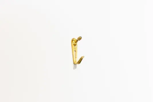 A single brass picture hook is mounted on a white wall.