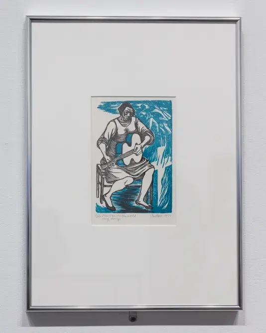 A framed print hanging on a wall shows a Black woman—rendered mostly in black ink—seated in a chair playing guitar. To her right, two images emerge from a swirling blue background: a hooded figure leans forward to assail another figure, and flames shoot upwards from a cross.