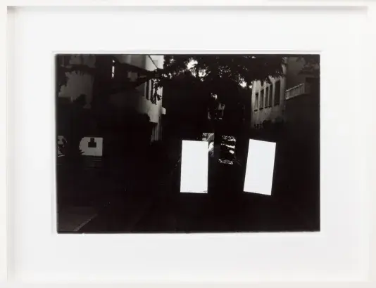 Black and white photograph of a dim street view at night in a white frame with a white matte. There are two stark white vertical rectangles on the right side of the image.
