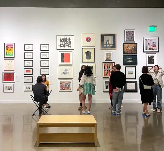 A group of people standing in pairs lined up near the wall of an open room that has artworks hung in salon style on all walls.