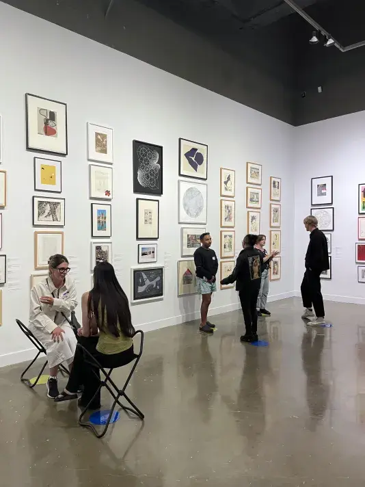 A group of people standing in pairs lined up near the wall of an open room that has artworks hung in salon style on all walls.