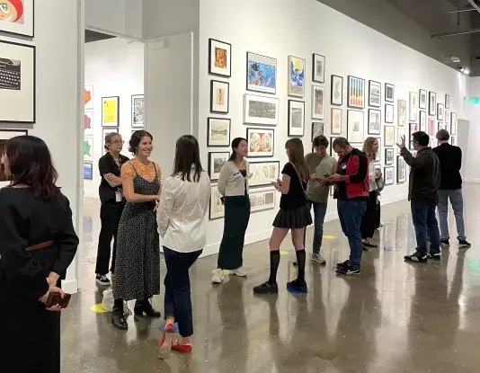 A group of people standing in pairs lined up near the wall of an open room that has artworks hung in salon style on all walls.