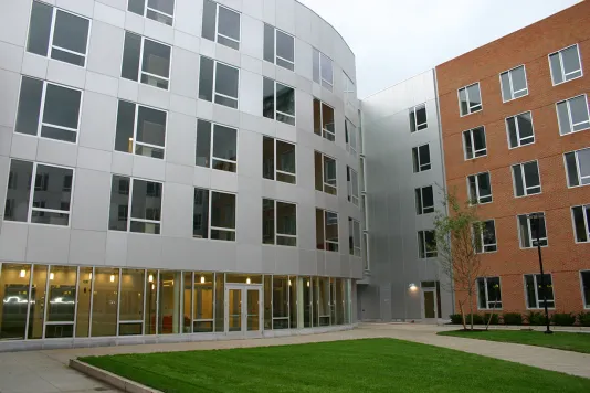 Silver building with lots of windows connected to a brick section of the building situated behind a green lawn.