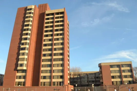 Red brick and beige building featuring a bright blue sky in the background and sun lighting up the building.