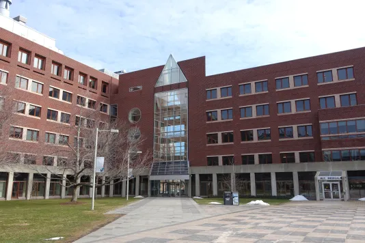 Red brick building with lots of windows and a glass atrium in the center with a pyramidal top.