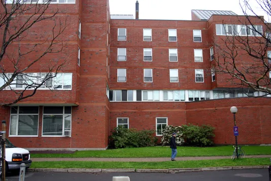 Red brick building behind a green lawn and a man walking on the sidewalk.