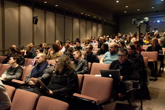 A group of people are seated in an auditorium during an event looking toward the stage.