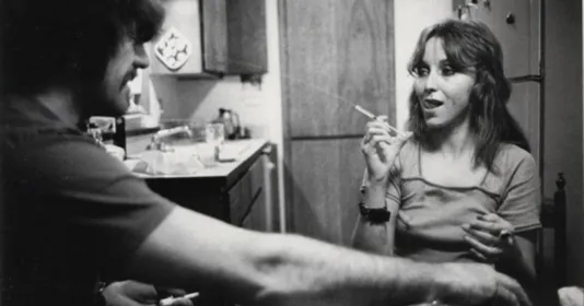 A black and white photo of a girll smoking a cigarette and a man in a flannel shirt.