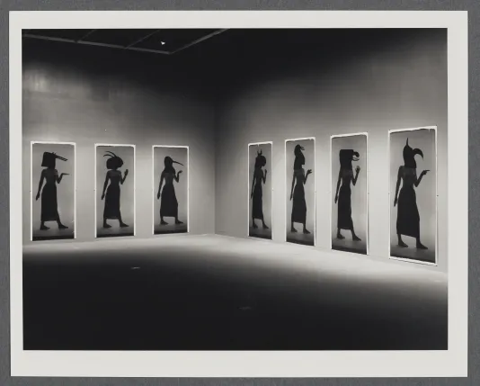 Black and white image of large scale polaroids of figures posed as Egyptian hieroglyphics.