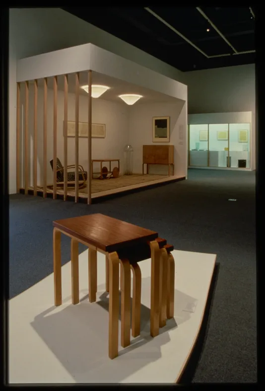 A set of end tables are shown in the foreground. Behind them is a mock-up of a room with sculptural furniture.