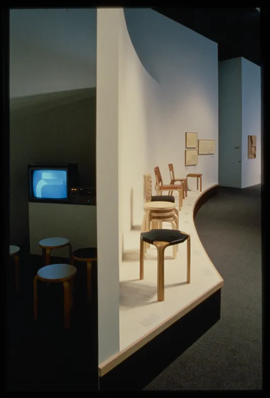 A gallery wall splits the image in half. One side shows sculptural chair designs and the other shows a space to view film.