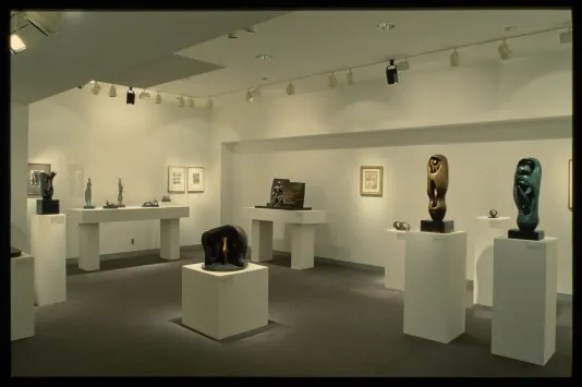 Pedestals hold a variety of figurative sculptures. Figurative drawings are shown on the gallery walls behind the sculptures. 