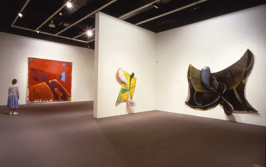A person views large abstract paintings in a gallery, 2 are odd shapes with the canvases extending outward casting shadows.