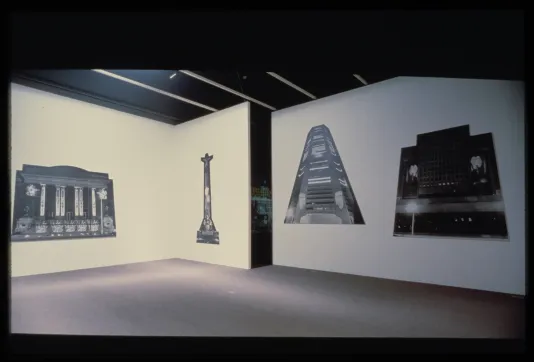Four large cut-outs of black and white monuments hang adjacent on three walls.