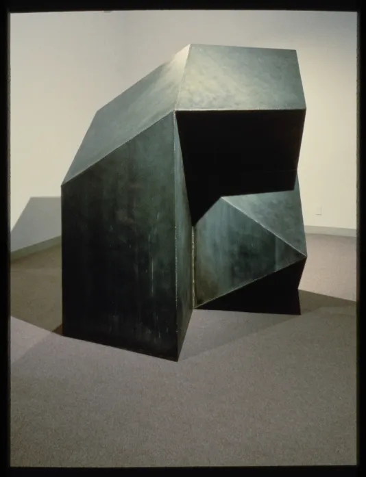 Large, black, metal, geometric sculpture sits in the corner of a gallery.