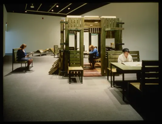Three visitors sit at tables and in cubicles while looking through reading materials like newspapers.