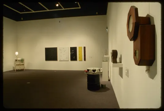 An installation view of hanging works and sculptures. Many sculptures take on the form of clocks, dials, or hourglasses.