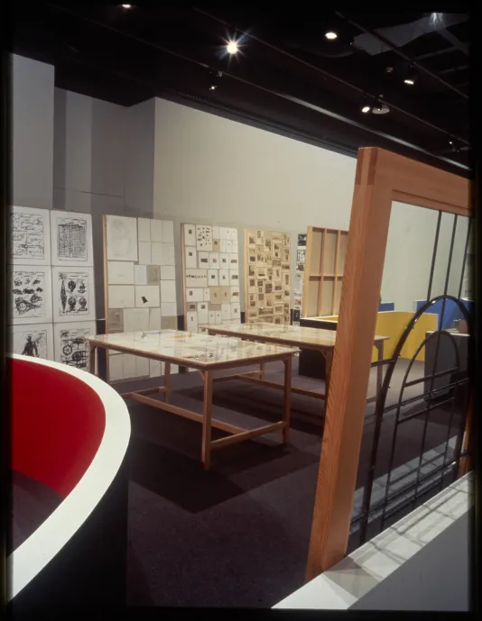 Tables inside the space display various objects as well as boards that stand vertically against the short gallery walls.