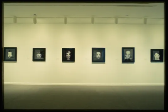 A row of black and white photographed portraits hang at eye level across the gallery wall. 